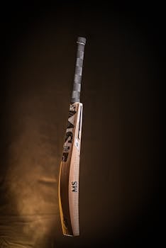 A high-quality wooden cricket bat suspended in a dark studio setting, showcasing its craftsmanship and design.